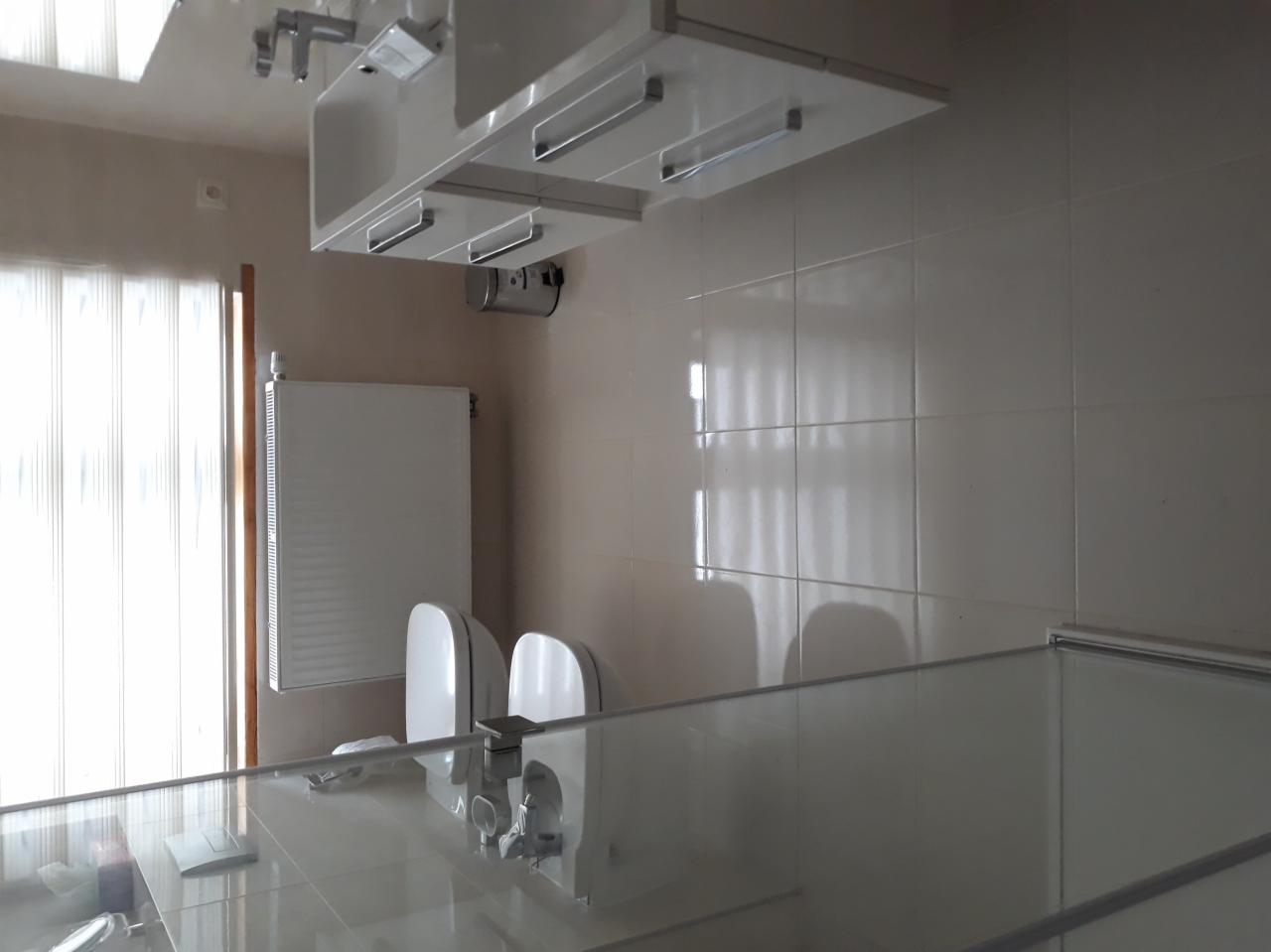 Wykończona łazienka z białymi płytkami, wiszącą szafką z oświetleniem, grzejnikiem i dwoma umywalkami z bateriami.