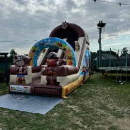 Piracki dmuchany zamek ze zjeżdżalnią, rozstawiony na trawie w Czarnej, z motywami piratów, palm i skrzyń ze skarbami. W tle widoczny słup z gniazdem ptaków i trampolina.