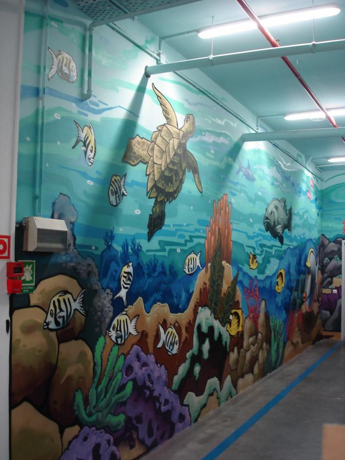 Ilustracja ścienna przedstawiająca podwodny świat z żółwiem morskim, rybami i koralowcami, w korytarzu oświetlonym lampami jarzeniowymi.