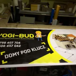 Baner reklamowy firmy Yogi-Bud z ofertą usług remontowo-budowlanych, numerami telefonów i hasłem 'Domy pod klucz', obok wizualizacja domu w trakcie budowy dachu na tle planów architektonicznych.