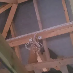 Instalacja elektryczna w przestrzeni poddasza: przewody przymocowane do drewnianej konstrukcji dachu, widoczne elementy izolacji.