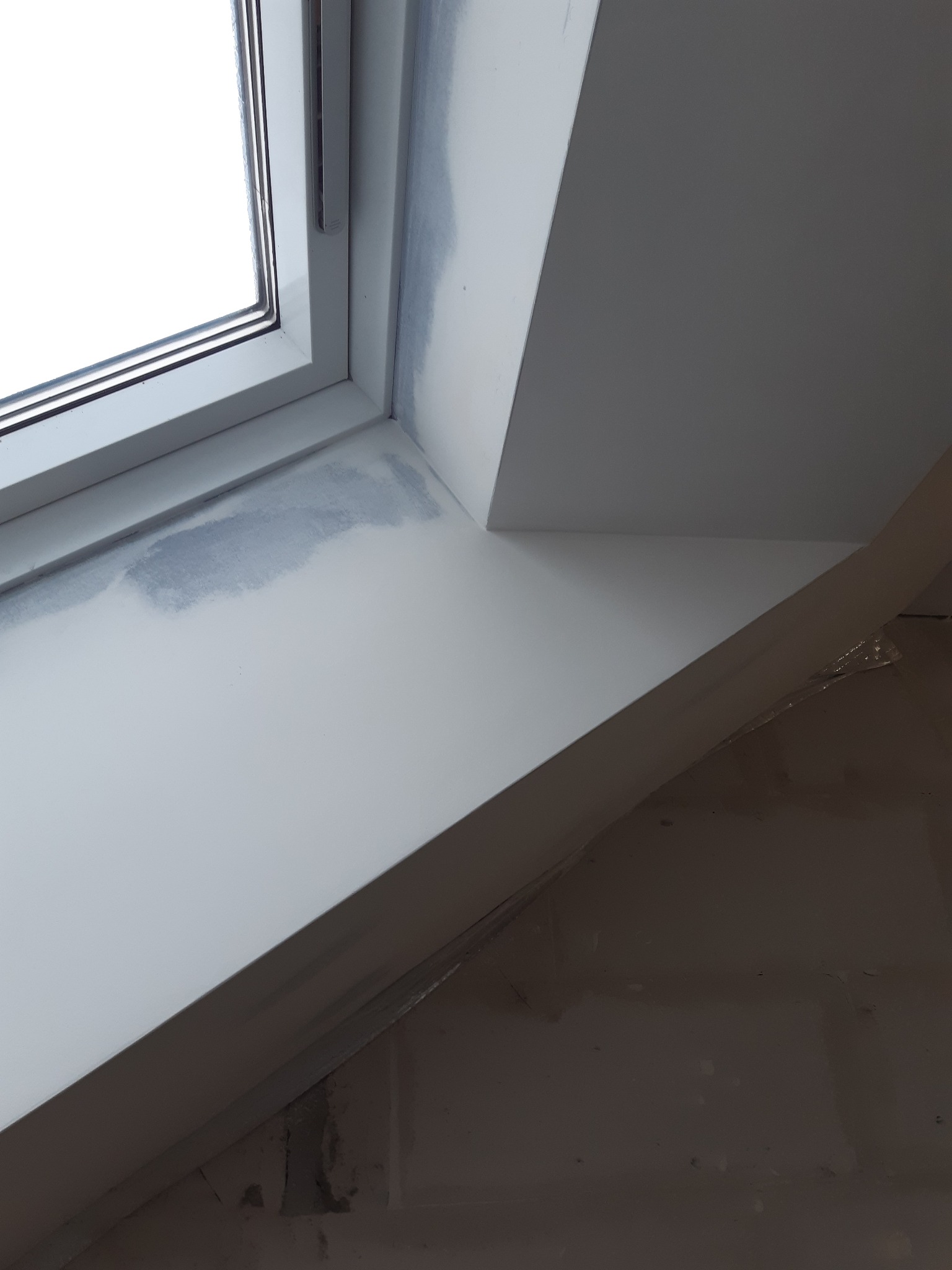 Wnętrze poddasza z oknem dachowym po szpachlowaniu, widoczne niedoskonałości i przygotowanie do malowania.