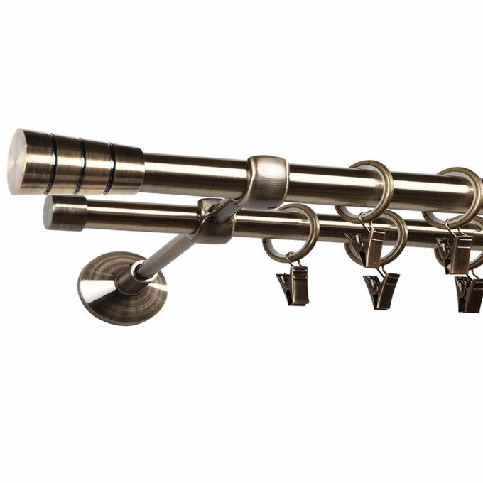 Podwójny karnisz w kolorze starego złota z pierścieniami i żabkami, zamontowany na ścianie.