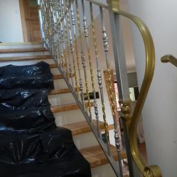 Dark Metal - Wnętrze domu w trakcie remontu: fragment drewnianych schodów zabezpieczonych czarną folią, z zamontowaną srebrno-złotą balustradą z ozdobnymi elementami.