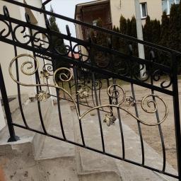 Dark Metal - Czarna balustrada schodowa z dekoracyjnymi, złotymi elementami roślinnymi, zamontowana przy wejściu do budynku w Rybnie.
