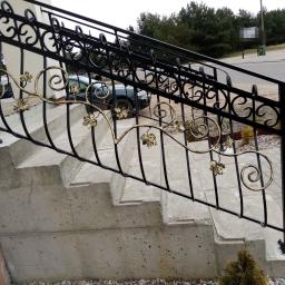 Dark Metal - Zewnętrzne schody z betonowymi stopniami i czarną, ozdobną balustradą z motywem liści w kolorze złota, widok z boku.