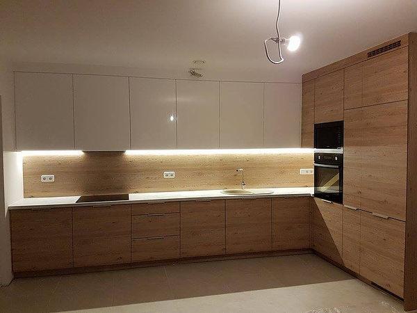 Nowoczesna kuchnia z białymi szafkami górnymi i drewnianymi szafkami dolnymi, podświetlona listwą LED, z wbudowanym piekarnikiem i mikrofalówką.