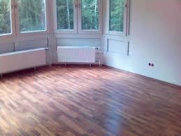 Wykończone wnętrze pokoju z parkietem ułożonym w jodełkę, widoczne okno z zielenią na zewnątrz i biały grzejnik pod nim.