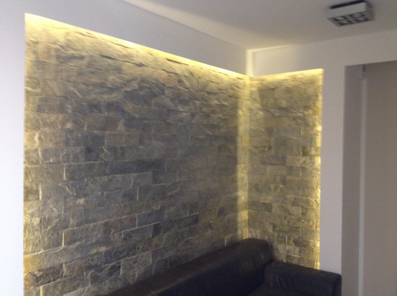 Ściana wykończona kamieniem dekoracyjnym z podświetleniem LED wzdłuż krawędzi, tworząca ciepłą atmosferę w salonie z fragmentem sofy w dolnej części kadru.