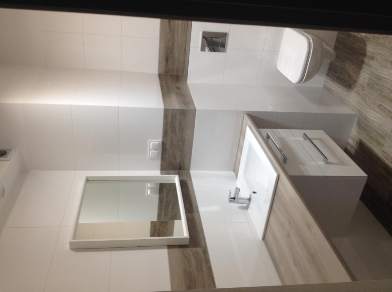 Nowoczesna łazienka z białymi płytkami, drewnopodobnymi akcentami, wiszącą toaletą, umywalką z szafką i prostokątnym lustrem.