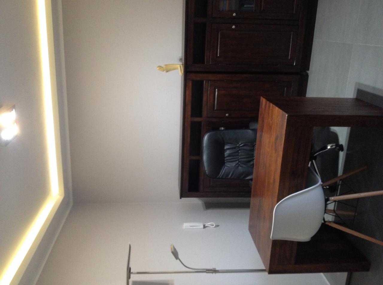 Ciemne drewniane meble biurowe: biurko z krzesłem i regał z czarnym fotelem biurowym, oświetlenie LED na suficie i lampka biurkowa.