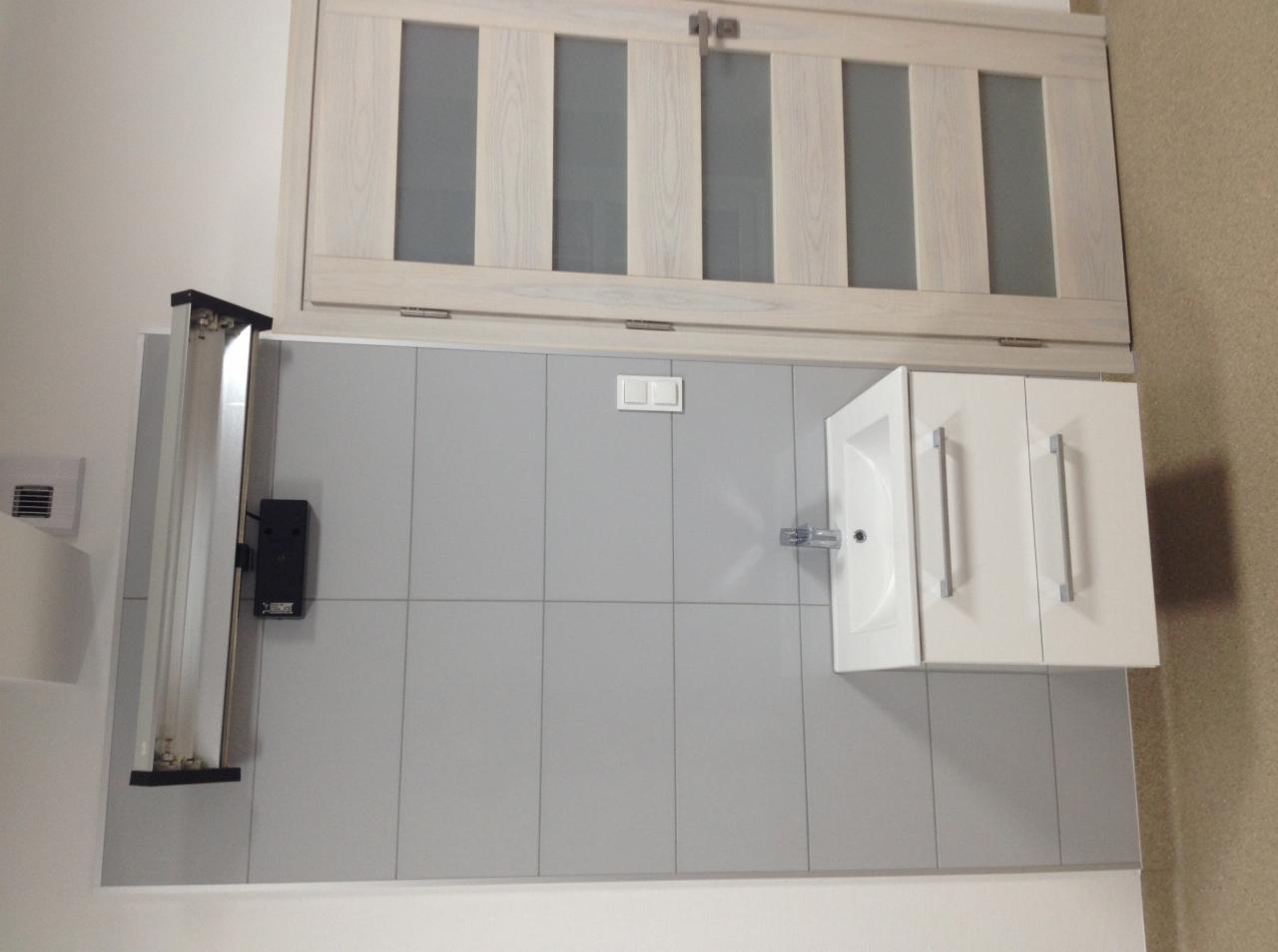 Nowoczesna łazienka z szarymi płytkami, białą szafką z umywalką, drewnianą szafką wiszącą i oświetleniem LED.