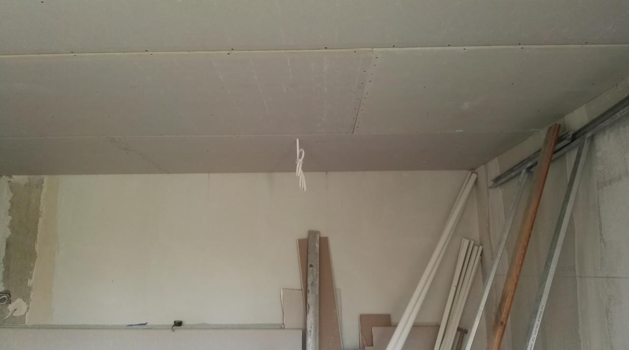 Montaż płyt gipsowo-kartonowych na suficie, widoczne profile metalowe i przewody elektryczne zwisające z otworu.