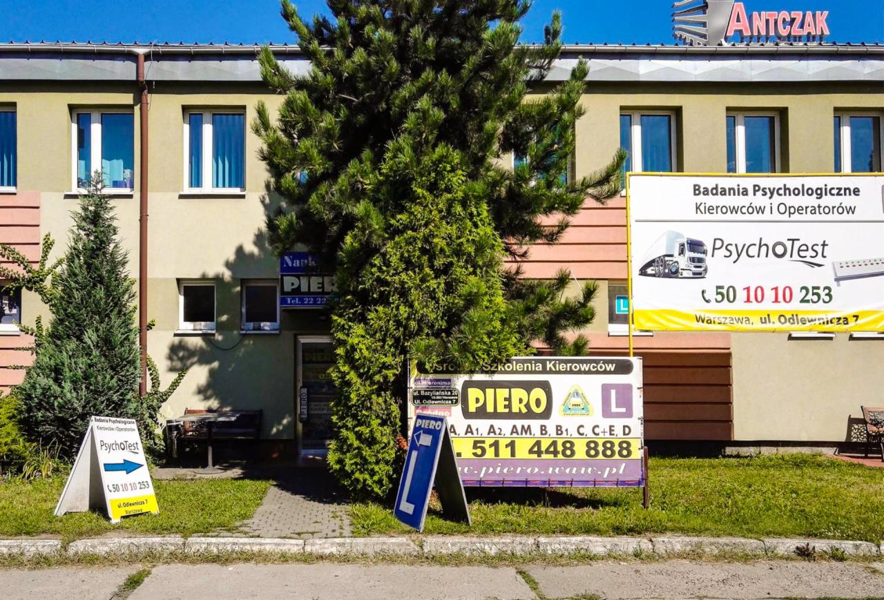 Budynek z szyldami szkoły jazdy i pracowni psychologicznej, z widocznymi tablicami informacyjnymi o badaniach psychologicznych kierowców i kursach nauki jazdy.