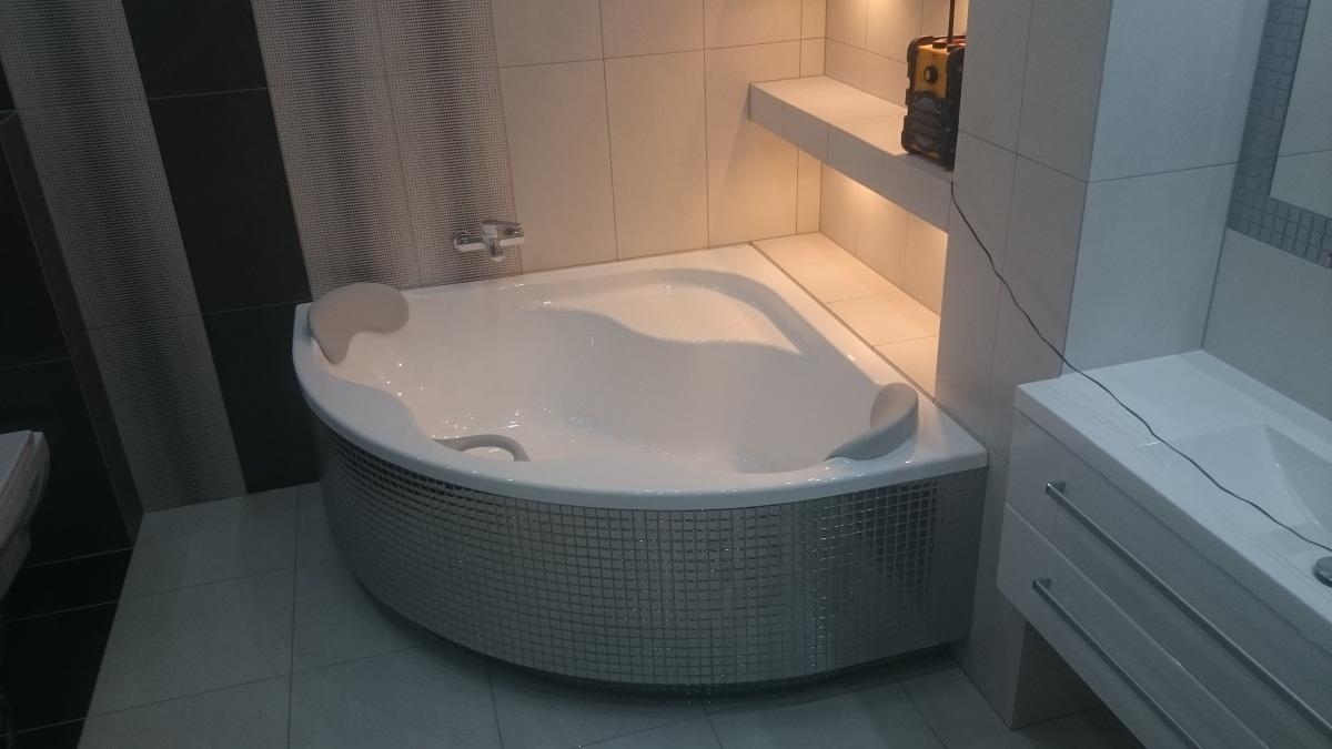 Narożna wanna obudowana mozaiką w wyremontowanej łazience, widoczna umywalka z szafką, czarno-białe płytki na ścianie i podświetlona półka z narzędziami.