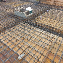 TOKU Projekt - Zbrojenie stropu z betonu, widok z góry na siatkę zbrojeniową na deskowaniu, Pyszkowo. Na środku betonowa skrzynka z dokumentacją budowlaną.