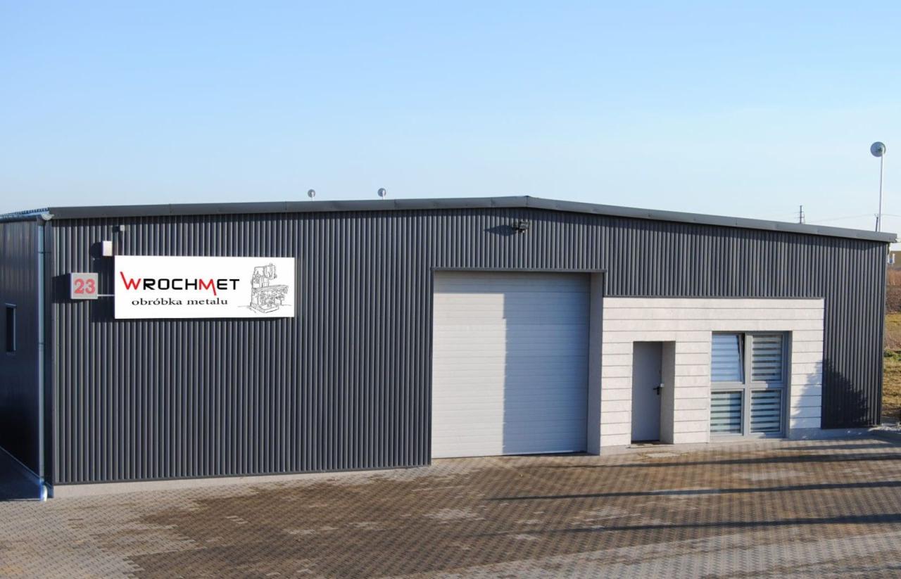 Budynek firmy WROCHMET zajmującej się obróbką metalu, z widocznym logo i numerem 23 na elewacji, szara blacha falista, biała brama garażowa i okno z żaluzjami.