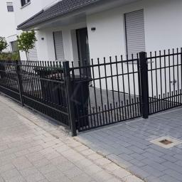 MDJ Metalltechnik Dawid Janczyk - Czarne, metalowe ogrodzenie z bramą wjazdową, otaczające posesję z nowoczesnym, białym domem w tle.