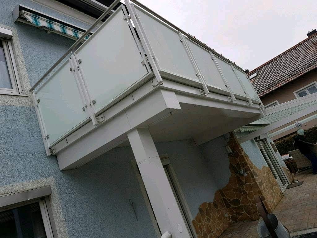 Nowoczesny balkon z balustradą ze szkła matowego i stalowych poręczy, widok z dołu, element elewacji budynku z oknami i roletami.