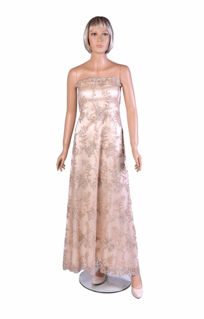 Beżowa suknia wieczorowa bez ramiączek, zdobiona srebrzystym, kwiatowym haftem, prezentowana na manekinie z blond peruką na białym tle.