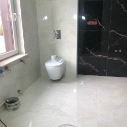 euro-S - Nowoczesna łazienka w trakcie wykańczania: białe i czarne marmurowe płytki, wisząca toaleta, widoczne narzędzia i wiadro z zaprawą.