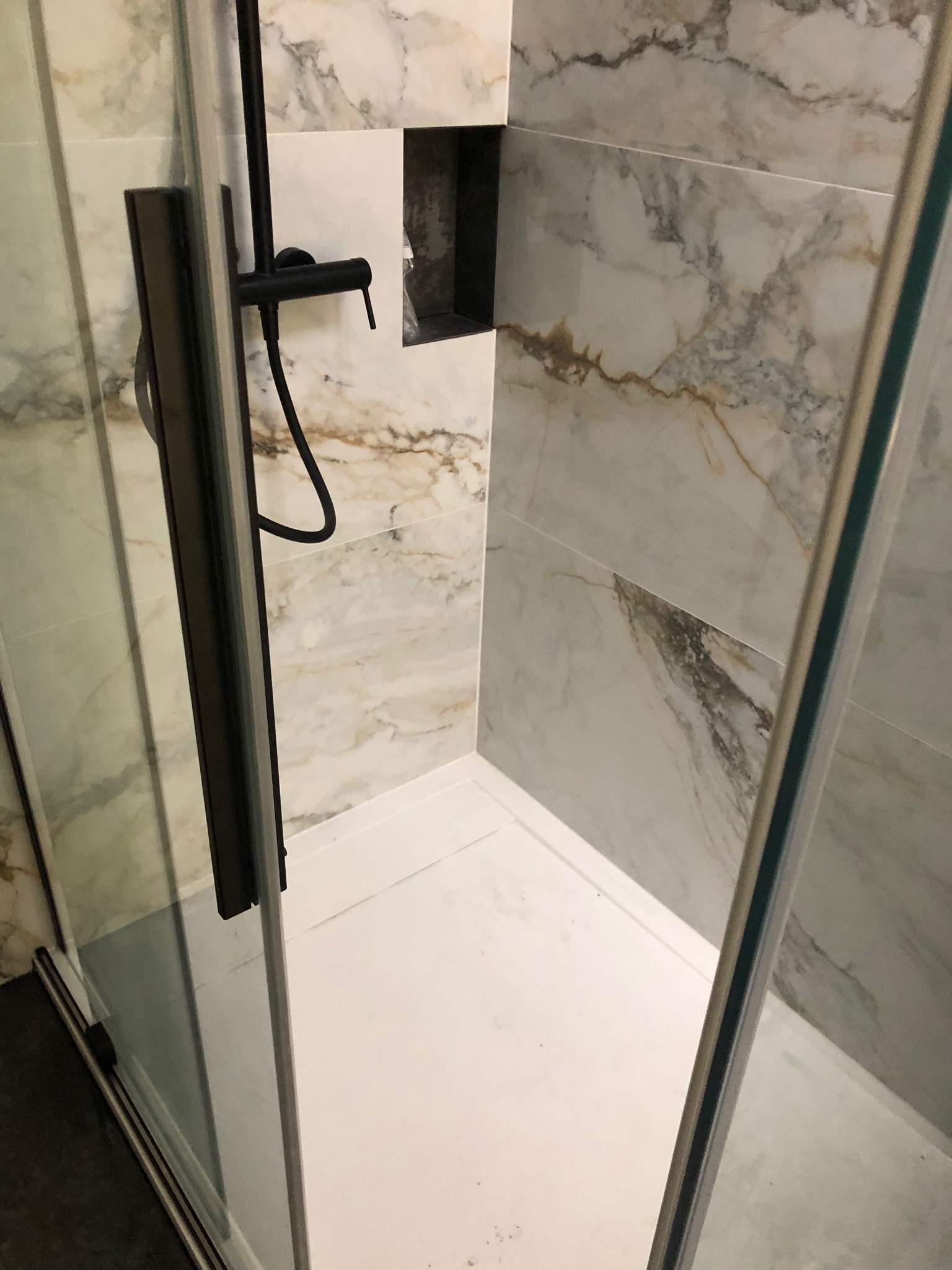 Nowoczesna kabina prysznicowa z czarną armaturą i marmurowymi płytkami ściennymi z wnęką.