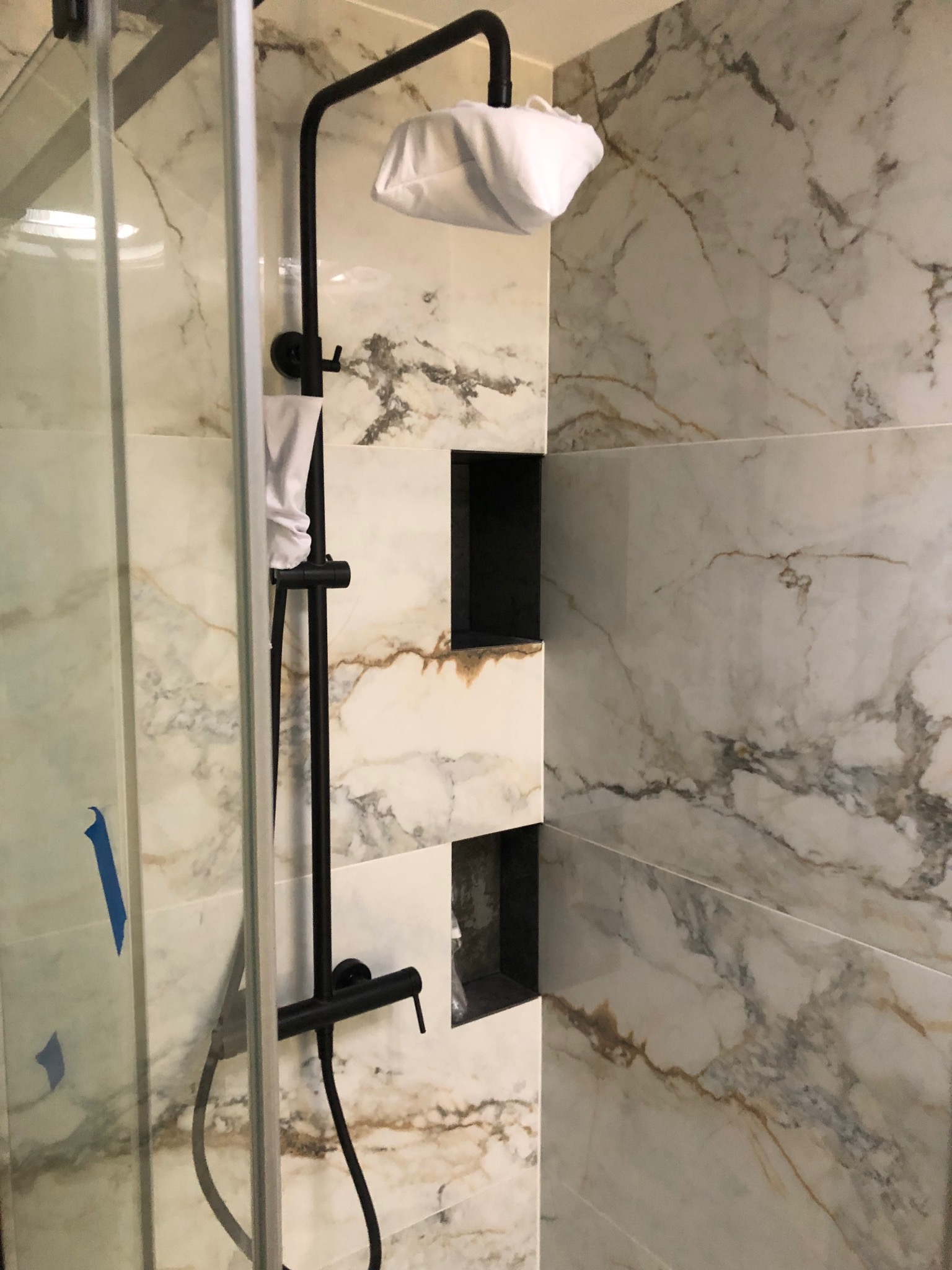 Nowoczesna kabina prysznicowa z marmurowymi płytkami, czarną armaturą i wnękami w ścianie.