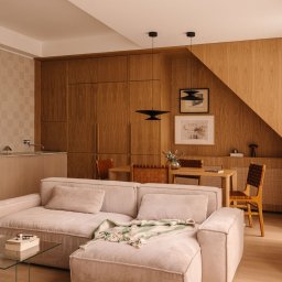 Averit Sławomir Pawłowski - Drewniana zabudowa ściany z szafkami i blatem, wkomponowana w skos dachu. Wnętrze dopełnia sofa, stół z krzesłami i lampy wiszące. Całość utrzymana w ciepłej, naturalnej kolorystyce.