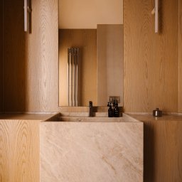 Averit Sławomir Pawłowski - Nowoczesna łazienka z umywalką z beżowego marmuru, drewnianą zabudową i minimalistycznym oświetleniem. W lustrze odbija się grzejnik.