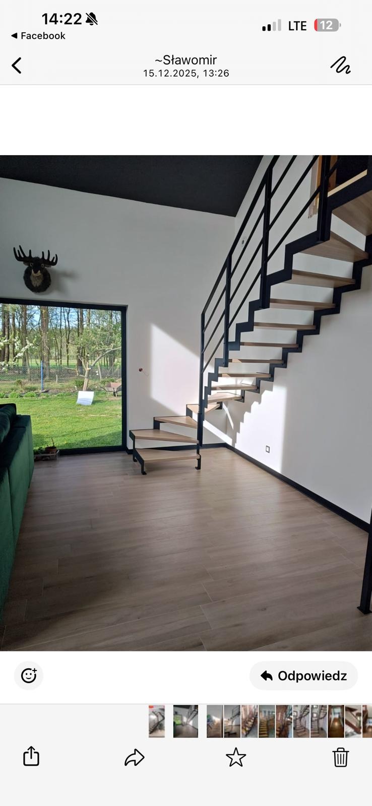 Nowoczesne schody z drewnianymi stopniami i czarną metalową balustradą w jasnym wnętrzu domu z widokiem na zieleń przez duże okno.