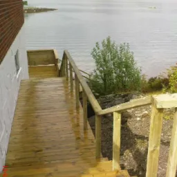 Drewniany taras z balustradą schodzący w dół w kierunku jeziora, widok na odległe miasto na wzgórzach, lekko deszczowa pogoda.