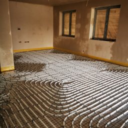 Grupa E-Vento - Rozłożona instalacja ogrzewania podłogowego na siatce w surowym pomieszczeniu z dwoma oknami przed wylewką.