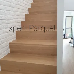 Jasne, drewniane schody z dębowymi stopniami, przylegające do ściany z białej cegły, widok z dołu, nowoczesny design.