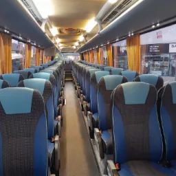 Wnętrze autobusu turystycznego Neoplan Tourliner z rzędami niebiesko-czarnych foteli, widok na przejście w kierunku przodu pojazdu, z widocznymi zasłonami w oknach.