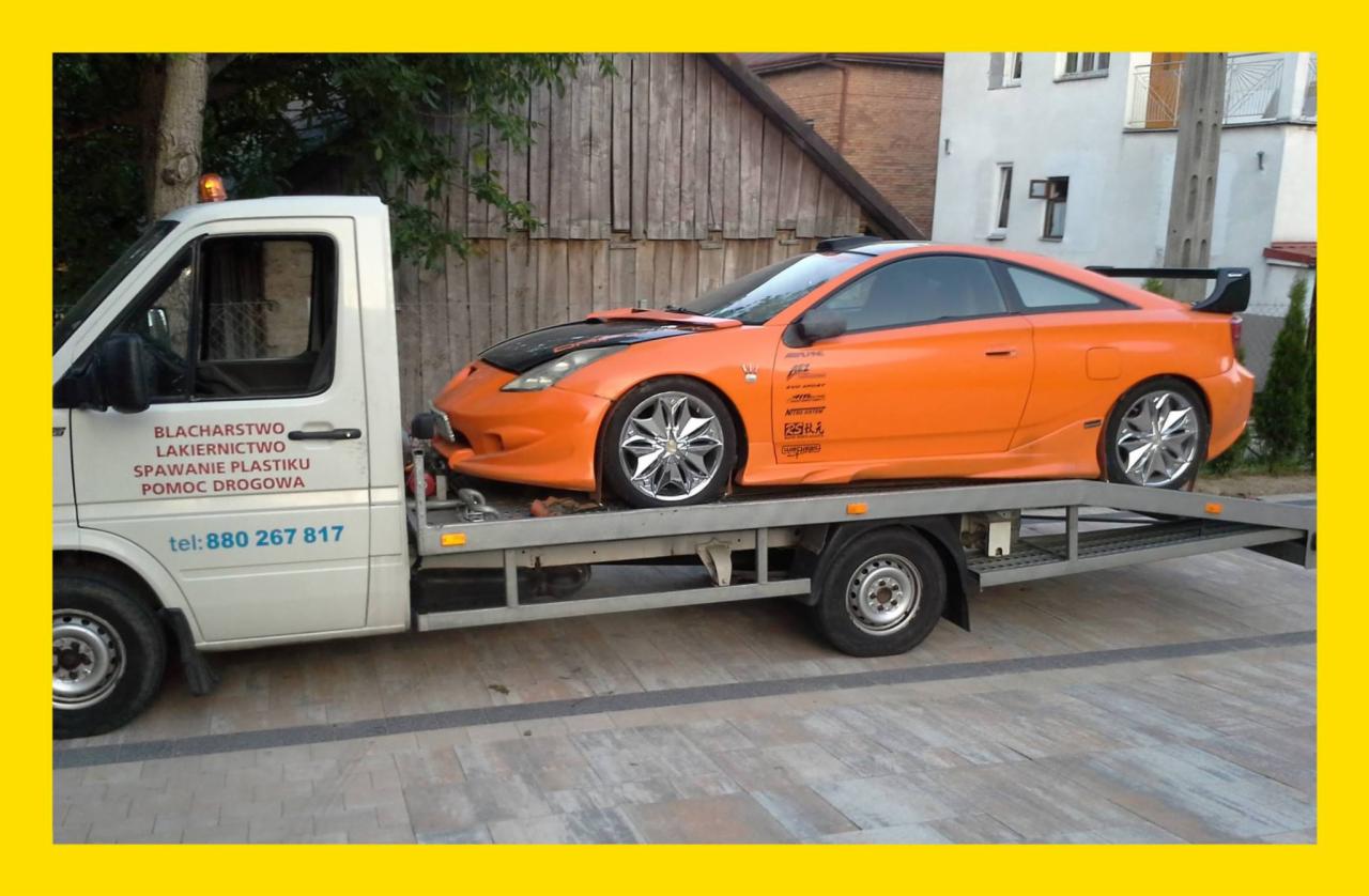 Pomarańczowe sportowe auto Toyota Celica z czarną maską i spojlerem, z chromowanymi felgami, przewożone na platformie białego pojazdu pomocy drogowej z napisem 'Blacharstwo Lakiernictwo Spawanie...