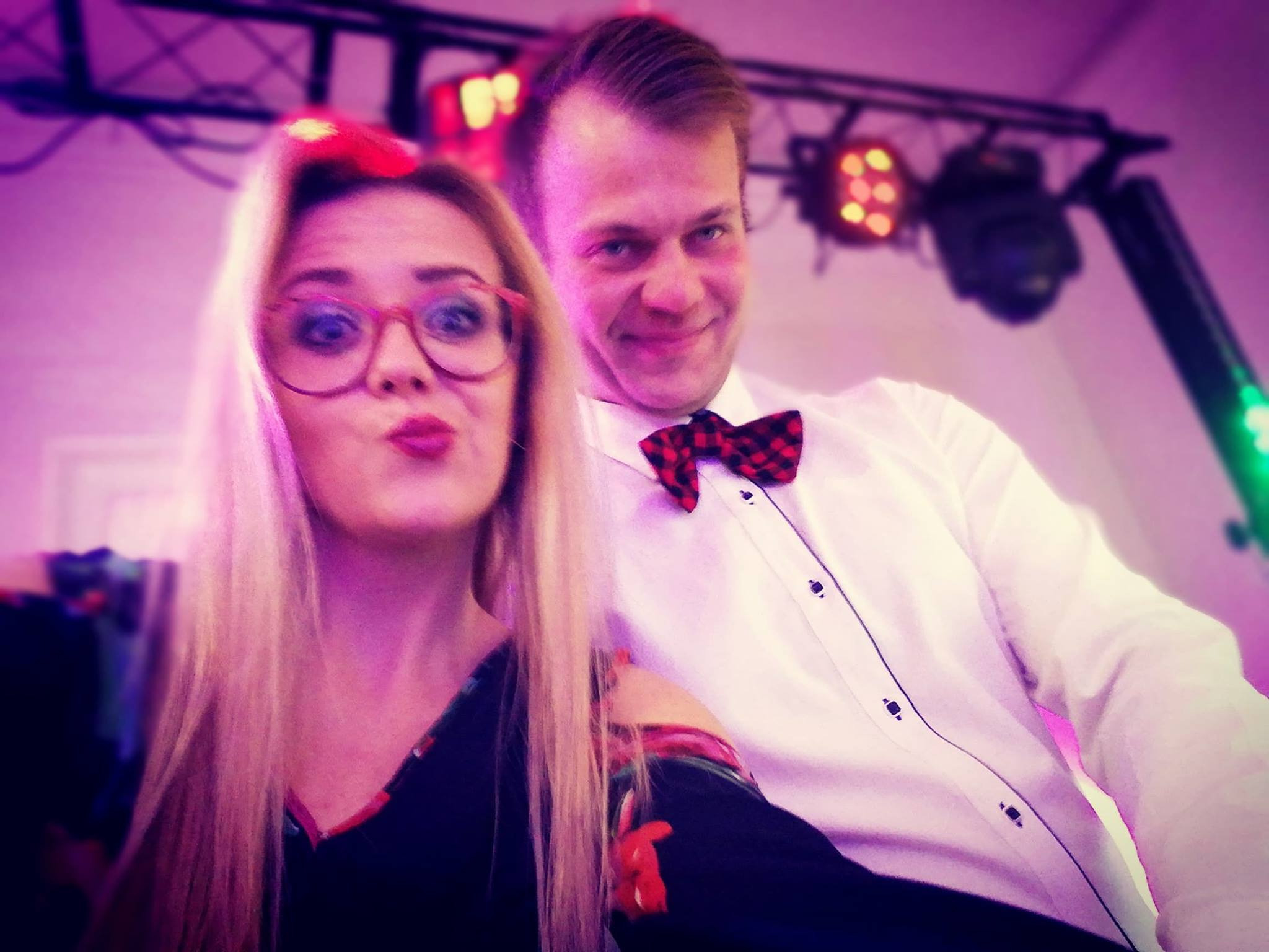 Portret kobiety w okularach i mężczyzny w muszce na tle sceny z oświetleniem, ujęcie z dołu.