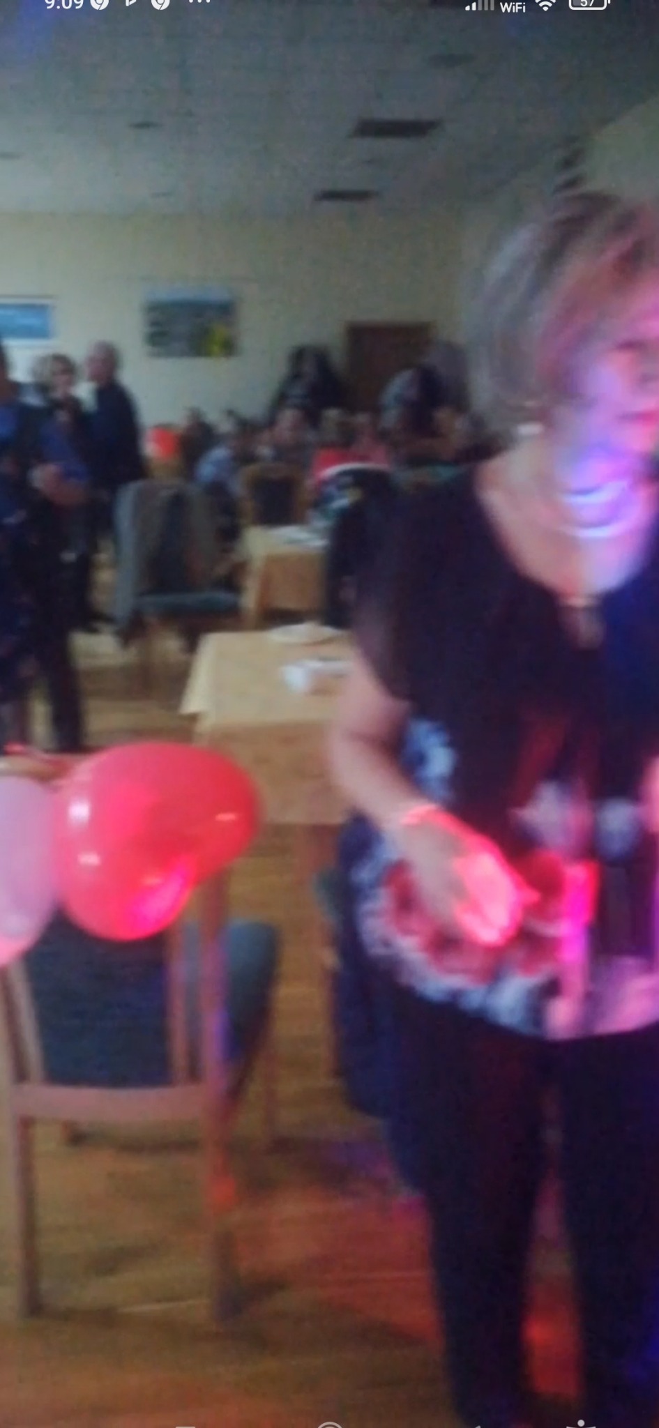 Sala bankietowa z gośćmi przy stołach, dekorowana balonami i oświetlona kolorowymi światłami, widok z perspektywy osoby stojącej na parkiecie.