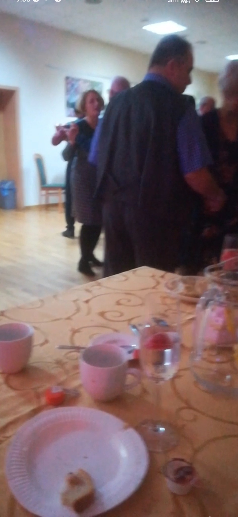 Uczestnicy zabawy tanecznej w pomieszczeniu, widoczny stół z naczyniami i resztkami jedzenia, ustawiony na pierwszym planie.