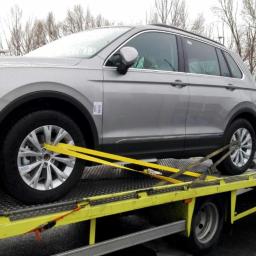 Prospect Arena SRL - Srebrny SUV marki Volkswagen zabezpieczony żółtymi pasami transportowymi na żółtej platformie lawety w trakcie załadunku, widok z boku na tle drzew i budynków.
