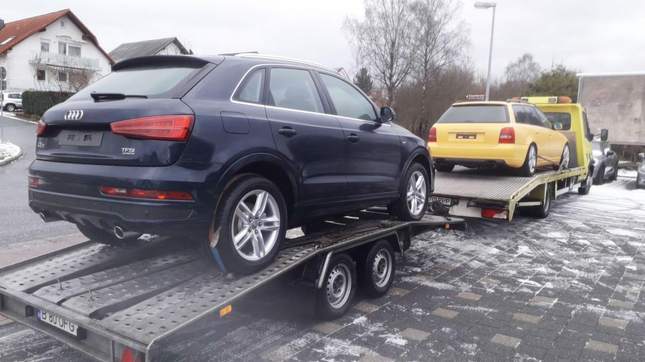 Granatowe Audi Q3 i żółte Audi A4 Avant na platformie lawety, widok z tyłu, na tle kostki brukowej z resztkami śniegu.