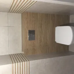 Wykończona łazienka z podwieszaną toaletą, brązowe płytki imitujące drewno na ścianie za toaletą i szarym przyciskiem spłukiwania, oraz szare płytki na pozostałych ścianach i podłodze,...