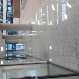 Długa, jasna posadzka z szarego kamienia w nowoczesnym budynku biurowym, widoczne szklane ściany i kolumny.