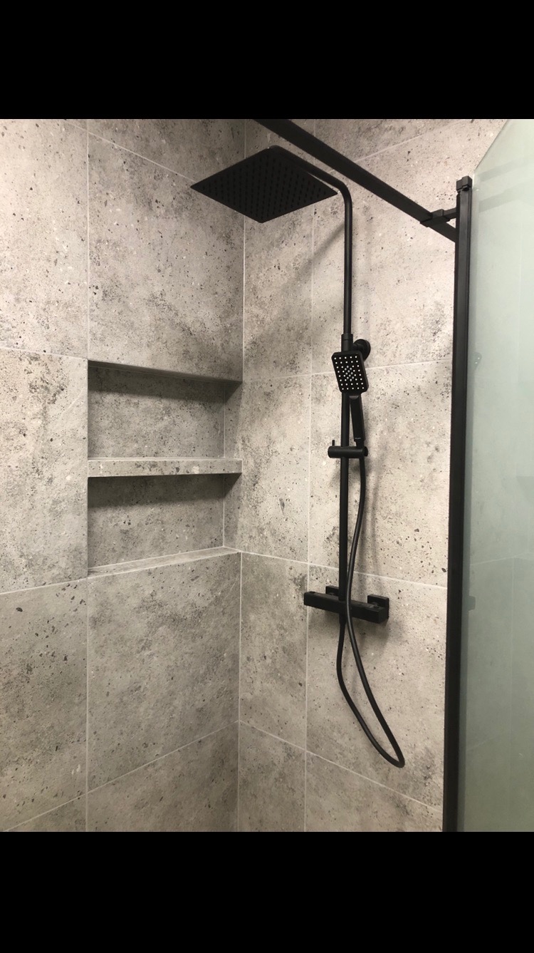 Wykończona kabina prysznicowa z szarymi płytkami, wnękami i czarną armaturą. Minimalistyczny design, nowoczesne wykończenie.