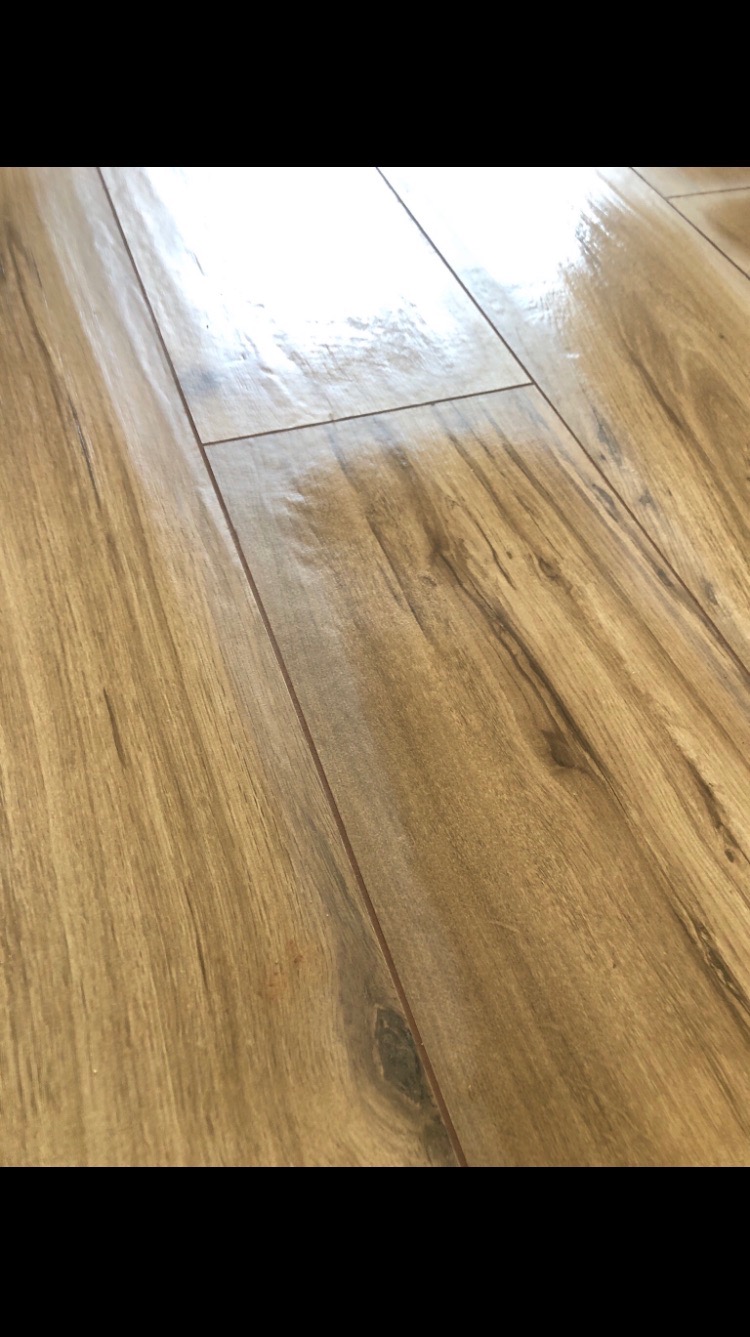 Połyskujące, ułożone panele podłogowe w odcieniach brązu, imitujące drewno. Widoczne delikatne usłojenie i łączenia między panelami. Ujęcie z niskiej perspektywy.