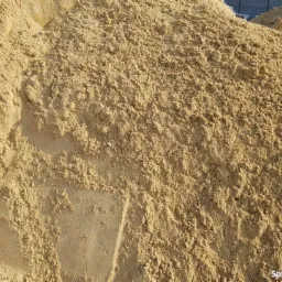 Duża pryzma drobnego, jasnobrązowego kruszywa budowlanego, prawdopodobnie przeznaczonego do prac wykończeniowych lub jako podsypka pod kostkę brukową.