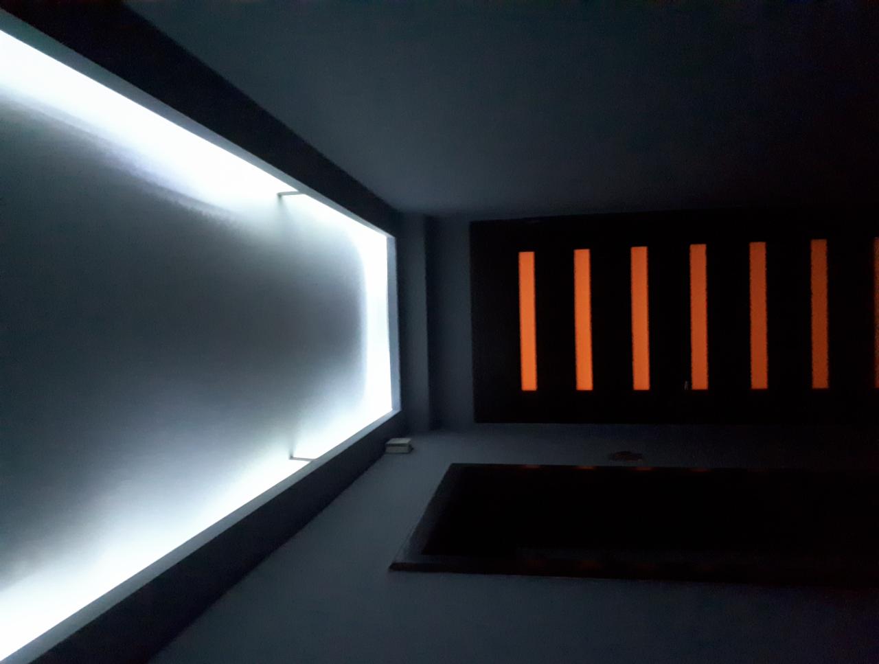 Nowoczesne wnętrze z podświetlaną ścianą i dekoracyjnym panelem z pionowymi, pomarańczowymi paskami, widok z dołu.