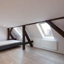 Jasne poddasze z drewnianymi belkami konstrukcyjnymi, łóżkiem z szarą ramą, grzejnikiem i dwoma oknami dachowymi.