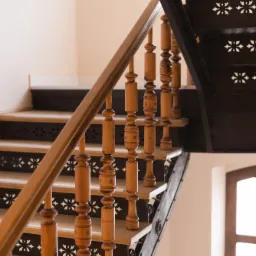Metalowe schody z drewnianymi stopniami i balustradą, ozdobione ażurowymi wzorami, widok z dołu.