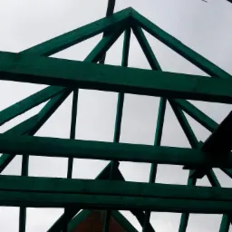 Konstrukcja dachu z impregnowanego drewna w kolorze zielonym, widok od dołu na tle pochmurnego nieba, w tle fragment muru z cegły i dach budynku.