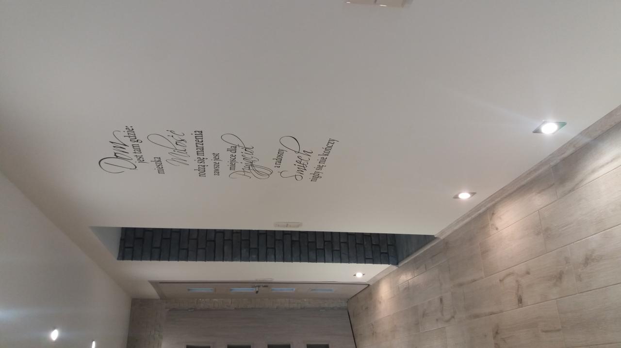 Biały sufit z napisem dekoracyjnym 'Dom jest tam gdzie mieszka Miłość rodzą się marzenia zawsze jest Przyjaciel a radosny Śmiech nigdy się nie kończy', wbudowane oświetlenie punktowe, fragment...